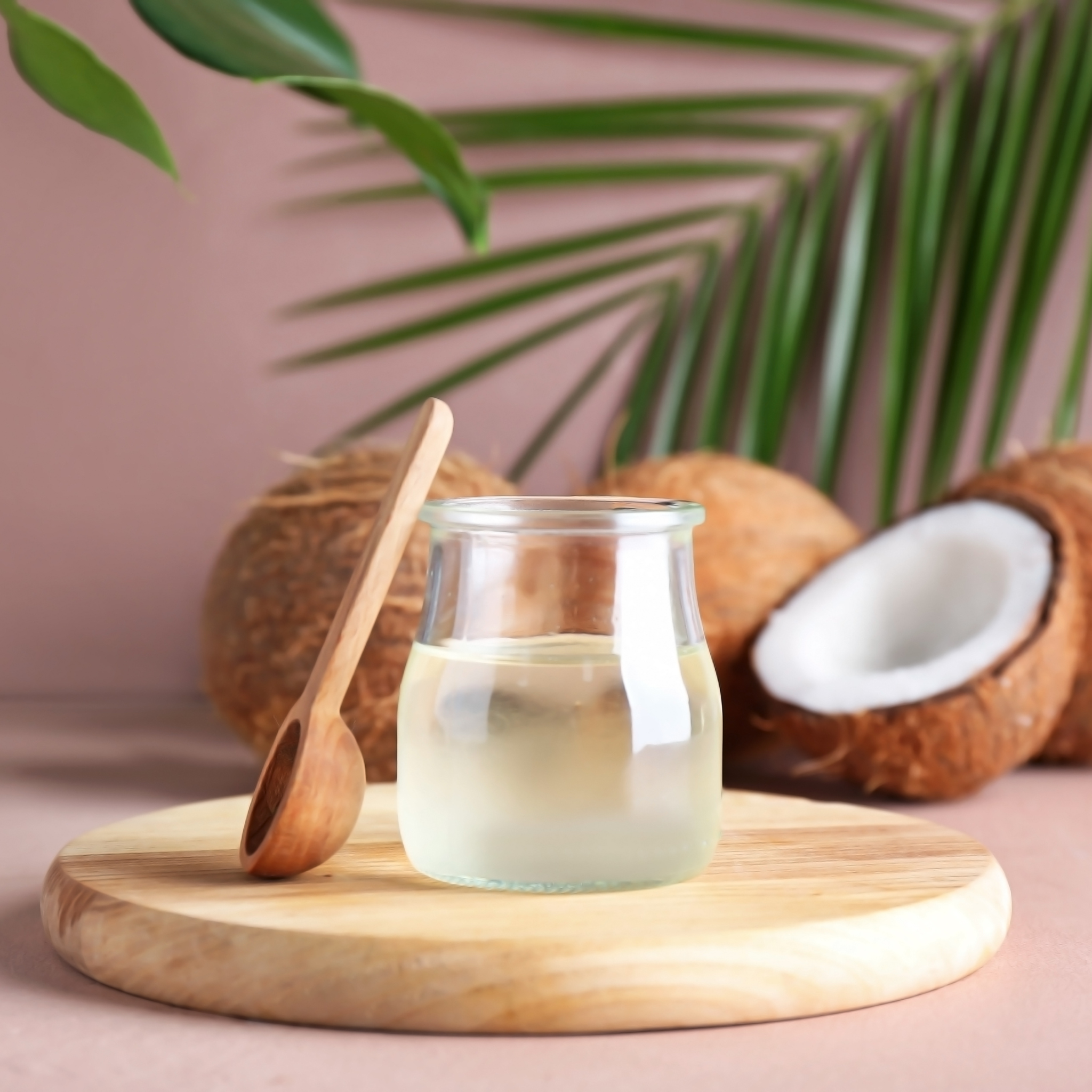 Ein Gläschen Kokosöl mit Kokosnüssen im Hintergrund